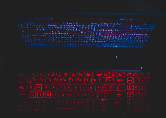 Dark-themed laptop setup with a red glowing keyboard and code on screen, ideal for tech enthusiasts.