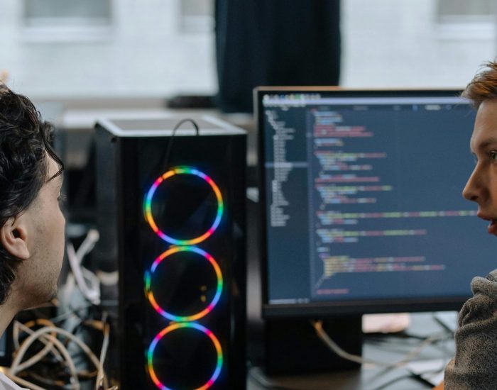 Two programmers discussing code on a monitor in a tech workspace, focusing on collaboration.